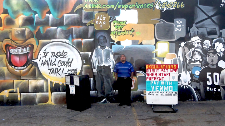 아트 디스트릭트 주차장 관리인이 주차장 그래피티에 그려진 자신의 그림 앞에서 포즈를 취하고 있다.
