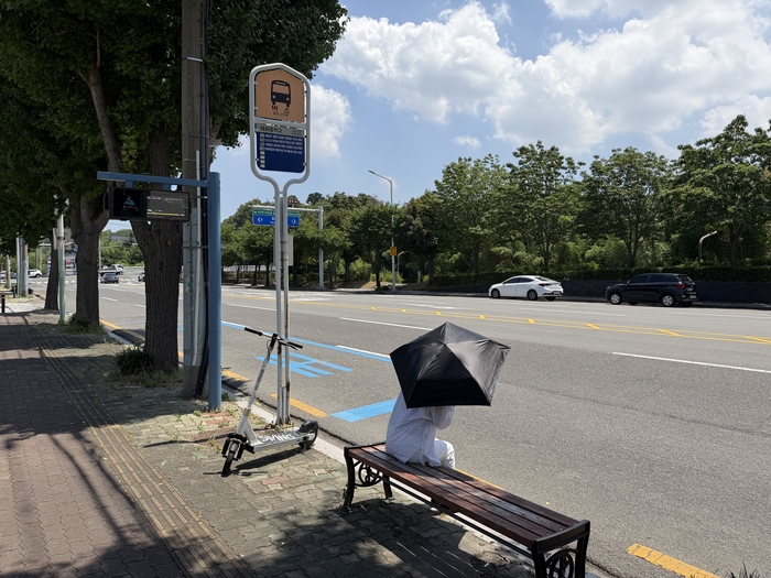 울산지역 버스정류소의 폭염 대응시설 보급률이 구·군별로 큰 차이를 보이는 가운데 동구의 승강장과 에어커튼 설치율이 가장 낮아 폭염 취약성이 두드러지는 것으로 나타났다. 사진은 22일 울산의 한 버스정류소. 지붕이나 그늘이 없어 양산 밑에서 무더위를 견디며 버스를 기다리는 모습.