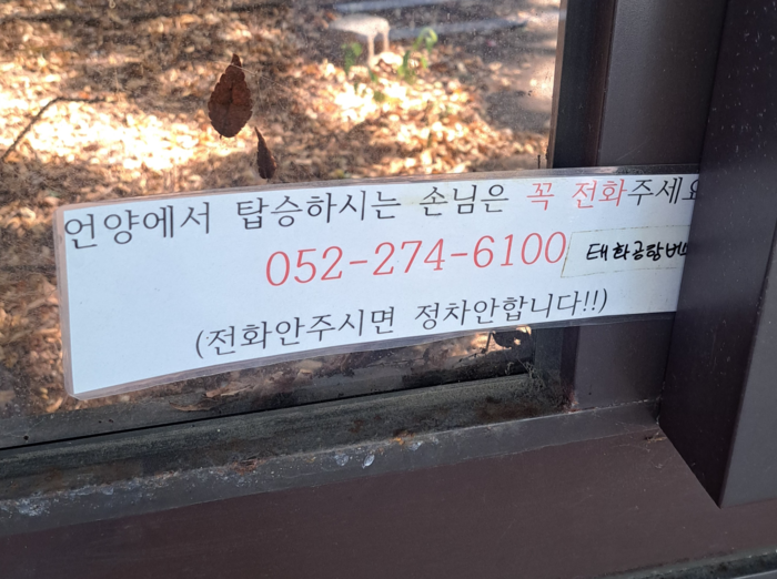 언양 서울산톨게이트 앞 정류장에는 울산~김해공항 버스 탑승객에게 업체로 전화해 달라는 안내문이 붙어 있다. 승객이 있을 때만 경유하는 방식이었지만, 업체 입장에서는 탑승객 확인과 운행 경로 조정이 필요하고 직행 승객은 추가 소요 시간을 감수해야 하는 구조다.